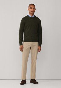 Dunkelgrüner Pullover mit Rundhalsausschnitt, kombiniert mit beigen Hosen. Braune Schuhe runden den Look ab und zeigen ein simples und sauberes Design.
