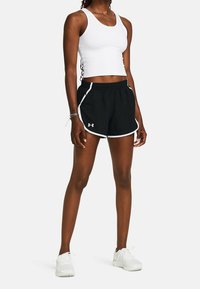 Svarta träningsshorts med vit kant, med elastisk midja och sidofickor. Bärs med en åtsittande vit linne och vita sneakers.