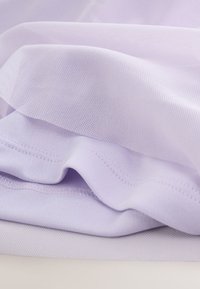 Gros plan d'un tissu violet clair montrant une texture tricotée et des coutures pliées sur un matériau textile doux.