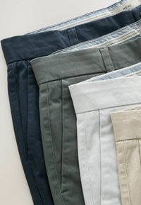 Patru perechi de pantaloni în nuanțe de albastru închis, verde olive, alb și bej. Toți au un design cu pliuri în față și benzi elastice contrastante cu detalii texturate.