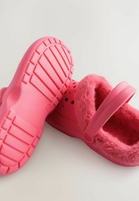 Vaaleanpunaiset pehmeät puukenkiä, joissa on pörröinen vuori, paksu pohja ja ranneke. Sisältää ilmanvaihtoaukkoja ja kuvioidun pohjan pidon parantamiseksi.