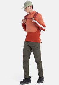 Felpa rossa e arancione con mezza zip, maniche lunghe e strisce bianche; abbinata a pantaloni cargo olivetti e stivali neri.