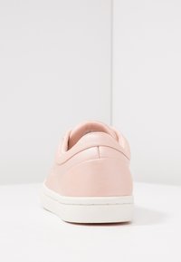 Baskets en cuir rose clair avec une forme arrondie, une texture lisse, un col rembourré et une semelle en caoutchouc blanche contrastante.