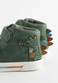 Zelené kožené boty s ilustrací krokodýla, zdobené vícebarevnými ostny na patě a bílou gumovou podrážkou s barevným pruhem.