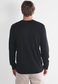 Camisa de manga larga negra hecha de algodón suave, con cuello redondo y una textura lisa. La parte posterior muestra costuras mínimas y sin gráficos.