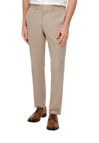 Pantalones de corte recto en color beige, elaborados con una tela suave, que presentan un ajuste slim, bolsillos laterales y un frente plano, combinados con zapatos de cuero marrón.