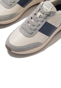 Baskets blanches et grises avec un upper en cuir lisse, des accents en daim gris et une bande bleu marine, des lacets texturés et une semelle en caoutchouc.