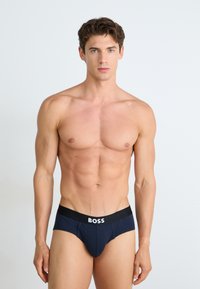Culotte bleu foncé avec une ceinture noire contrastante sur laquelle est inscrit le logo blanc "BOSS", tissu lisse, design ajusté et coutures minimales.