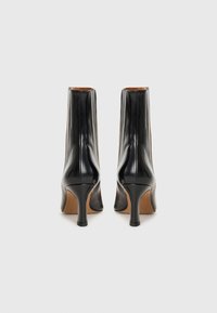 Bottines en cuir noir avec un design élégant, un talon stiletto haut et une texture lisse. Présente une construction minimaliste avec des coutures arrière.