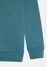Sweatshirt azul petróleo com bolso canguru, punhos e bainha canelados. Feito de tecido texturizado com um acabamento suave.