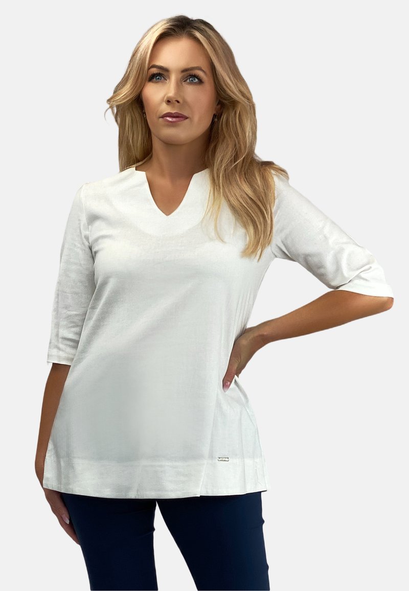 Biała bluzka z dekoltem w serek i rękawami o długości trzech czwartek, gładka w fakturze, z rozcięciem po boku. Posiada małe metaliczne logo na dolnym brzegu.