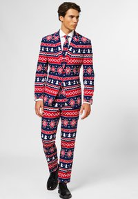 Rot, weiß und blau gemusterter Anzug mit Weihnachtsmotiven; enthält Schneeflocken und Bäume. Figurbetonter Stil mit passender Krawatte, kombiniert mit schwarzen Schuhen.