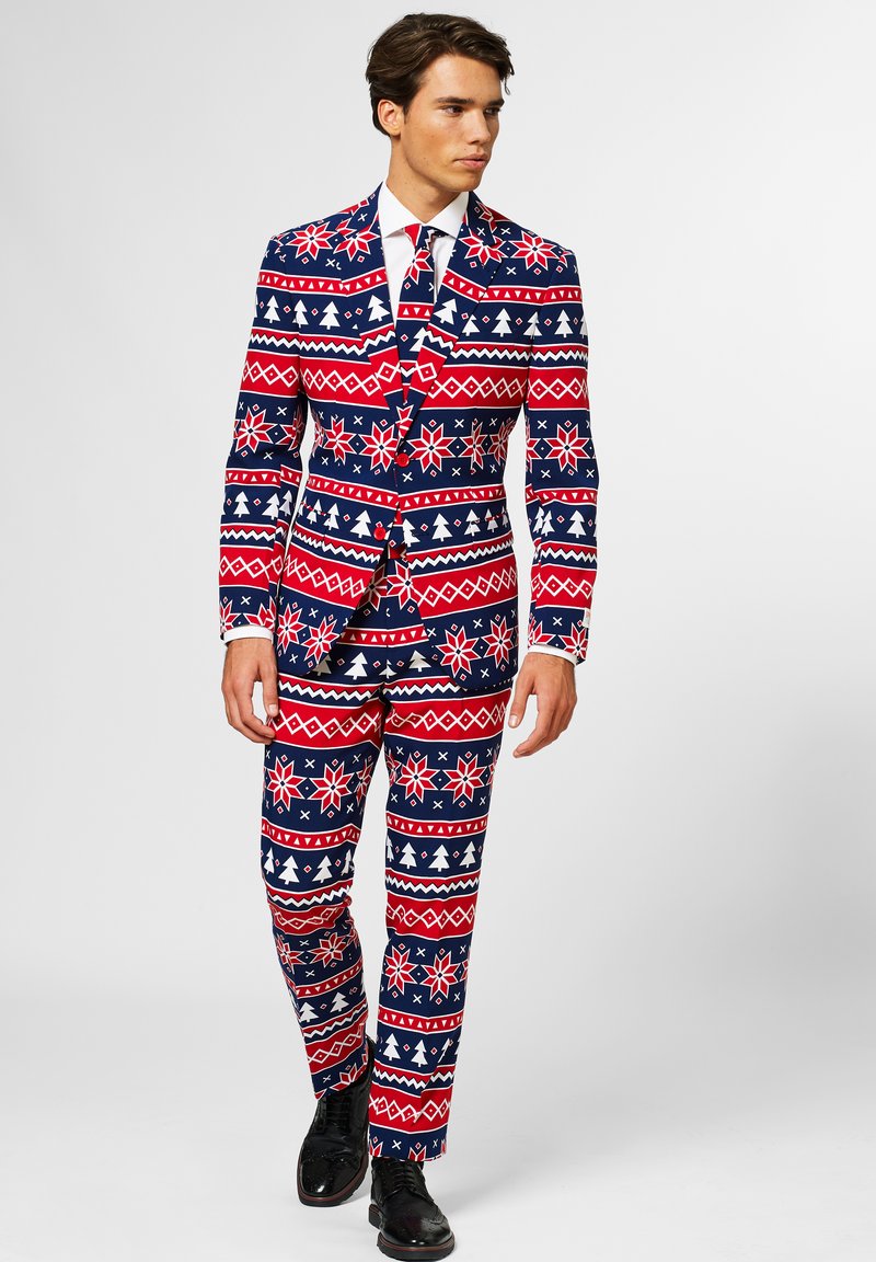 Rot, weiß und blau gemusterter Anzug mit Weihnachtsmotiven; enthält Schneeflocken und Bäume. Figurbetonter Stil mit passender Krawatte, kombiniert mit schwarzen Schuhen.