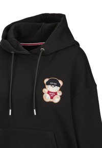 Zwarte hoodie met een pluche teddybeer borduring, een blauwe hoed en een rode "APRES SKI" shirt. Met trekkoorden en zilveren hardware.