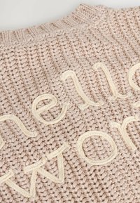 Hellrosa Strickpullover mit erhabener cremefarbener Schrift, die in den Stoff integriert ist. Strukturiertes Muster mit Rundhalsausschnitt.