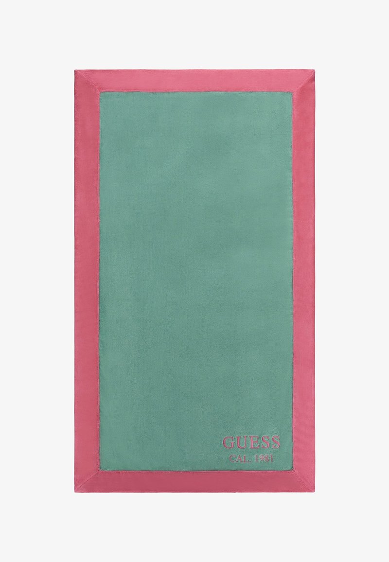 Asciugamano rettangolare con un centro verde e un bordo rosa. Realizzato in tessuto morbido con la scritta stampata "GUESS CAL 1981" nell'angolo in basso.