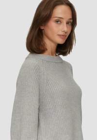 Lichtgrijze gebreide trui met een ronde hals, lange mouwen en een gestructureerd patroon. Materiaal lijkt zacht en knus.
