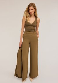 Olivengroene geribde tanktop met V-hals, gecombineerd met brede, high-waisted broeken in een bijpassende tint en beige puntige hakken.