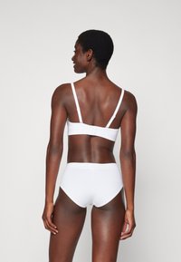 White seamless bralette with adjustable straps and hook closure, paired with white high-waisted briefs, displayed from the back. Smooth texture.