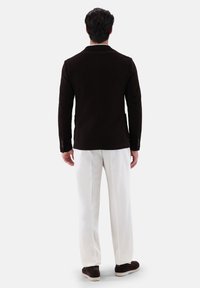Blazer in corda di colore marrone con vestibilità su misura, caratterizzato da un colletto a revers, due tasche e dettagli con bottoni argentati, abbinato a pantaloni bianchi.