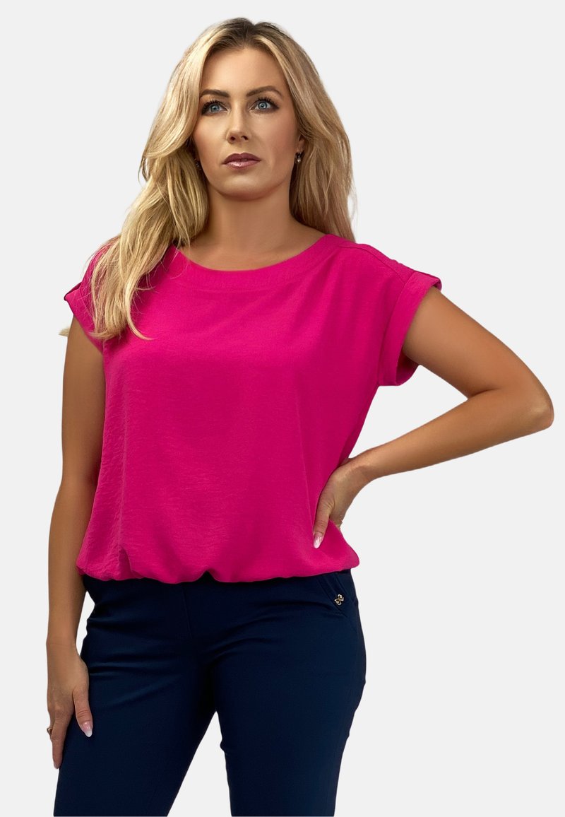 Fuksjowa bluzka z krótkim rękawem wykonana z lekkiego materiału, z okrągłym dekoltem i luźnym krojem; w zestawie z ciemnymi spodniami.