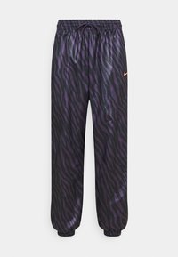 Pantaloni jogger con stampa zebra viola e nera, dotati di vita elastica e cordino. Presentano polsini elastici e un piccolo logo Nike arancione sul lato.