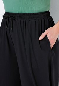 Svarta, lätta byxor med resårmidja och dragsko. Har sidofickor och en slät yta.