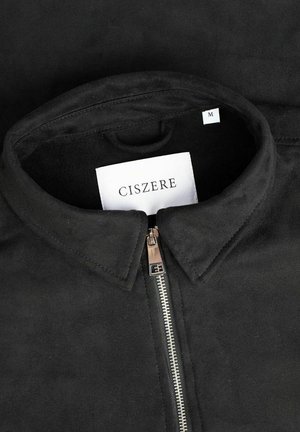 Svart mockajacka med dragkedja, krage och en etikett med texten "CISZERE" och storlek "M". Slät textur med minimala accenter.