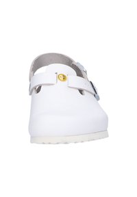 White clogs made of synthetic material with a rounded toe, adjustable strap, and rubber sole. Features a circular logo accent near the strap.