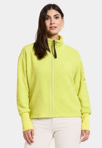 Fleece-pusero kirkkaan keltaisena, jossa on korkea kaulus, etuvetoketju ja istuvat hihansuut. Teksturoitu pinta ja rento malli.