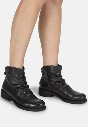 Stivali alla caviglia in pelle nera con un design svasato, punta rotonda e tacco basso impilato. Presentano dettagli con bottoni sul lato esterno.