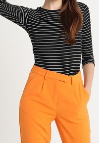 Svartvitt randig långärmad topp i kombination med högmidjade orange byxor. Byxorna har framveck och sidofickor.