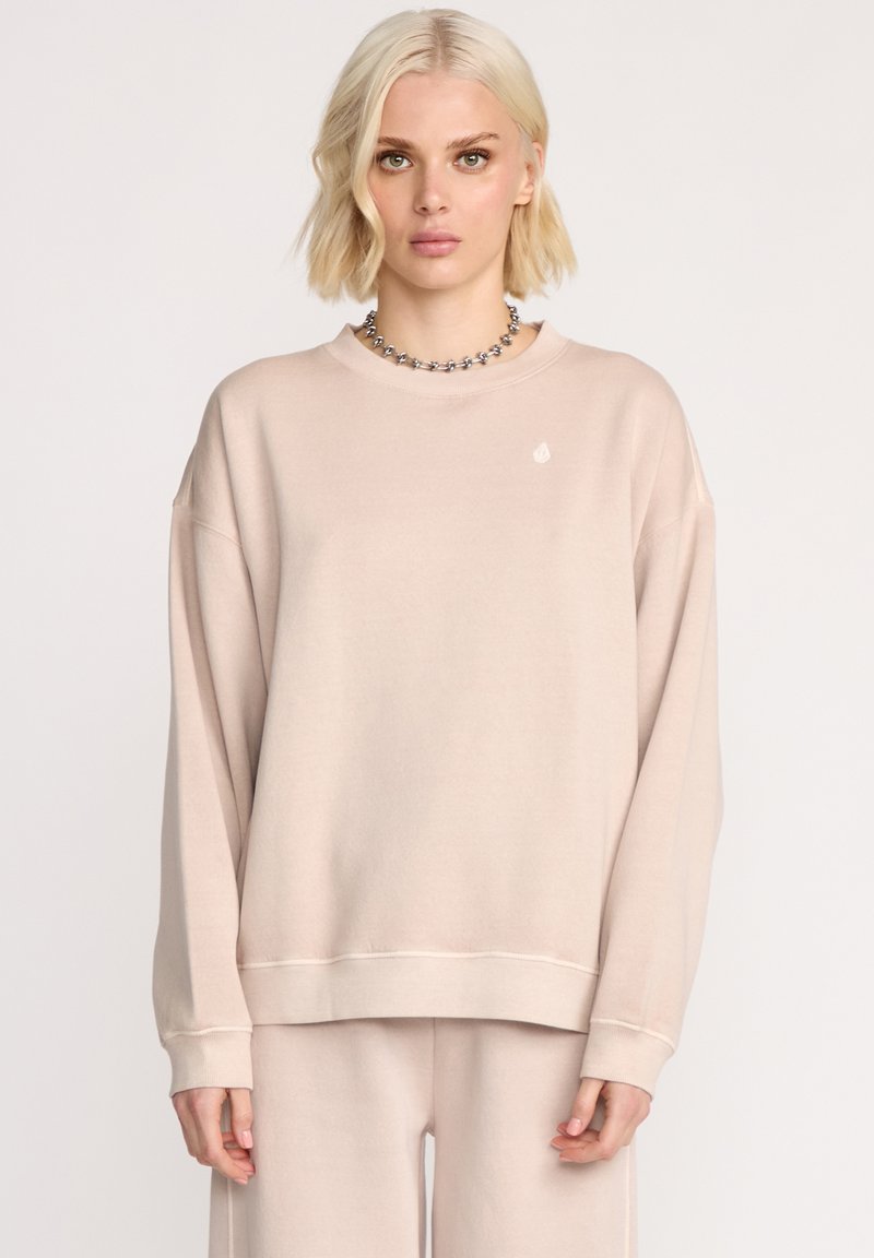 Sweatshirt beige clair avec une coupe ample, un col rond et des manches longues. Présente un petit logo sur la poitrine et des poignets côtelés.