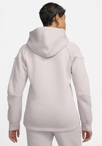 Lichtroze hoodie gemaakt van zachte stof, met een grote capuchon, lange mouwen en een relaxte, iets oversized pasvorm. Gladde textuur.