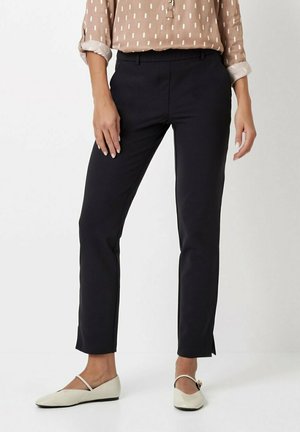Black slim-fit pants with a smooth texture and a tailored design. Featuring small side slits at the hem for added detail. Worn with light-colored shoes.