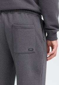 Grå sweatpants med en baglomme med et mærke, lavet af blødt stof, med en elastisk talje og en afslappet pasform.