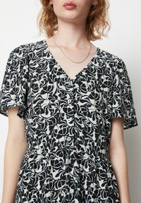 Abito con motivo floreale in bianco e nero, dotato di scollo a V, maniche corte, chiusura con bottoni e dettaglio della gonna arricciata.