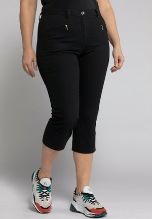 Pantaloni capri neri dal design aderente, con due tasche con zip e una superficie liscia. Abbinati a scarpe da ginnastica atletiche multicolori.
