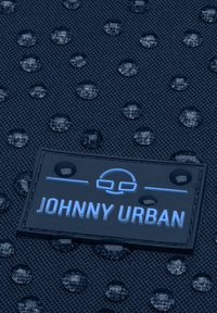 Námorná textúrovaná tkanina s vodnými kvapkami, so zreteľnou čiernou etiketu s nápisom "JOHNNY URBAN" modrým písmom, ktorá ukazuje trvácnosť.