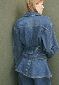 Giacca di denim con design peplum, lavaggio medio, colletto a punta, maniche lunghe e accessori in metallo. Presenta cuciture e tasche.