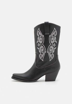 Bota vaquera negra hasta la mitad de la pantorrilla con costuras decorativas blancas en el cañón, tacón bloque y una pestaña para tirar en la parte superior.