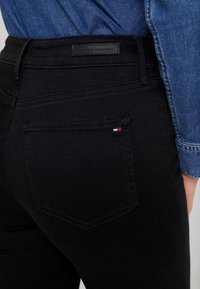 Vaqueros de mezclilla negros con corte recto, bolsillos traseros con detalles de costura y una etiqueta de cuero con marca en la cintura.