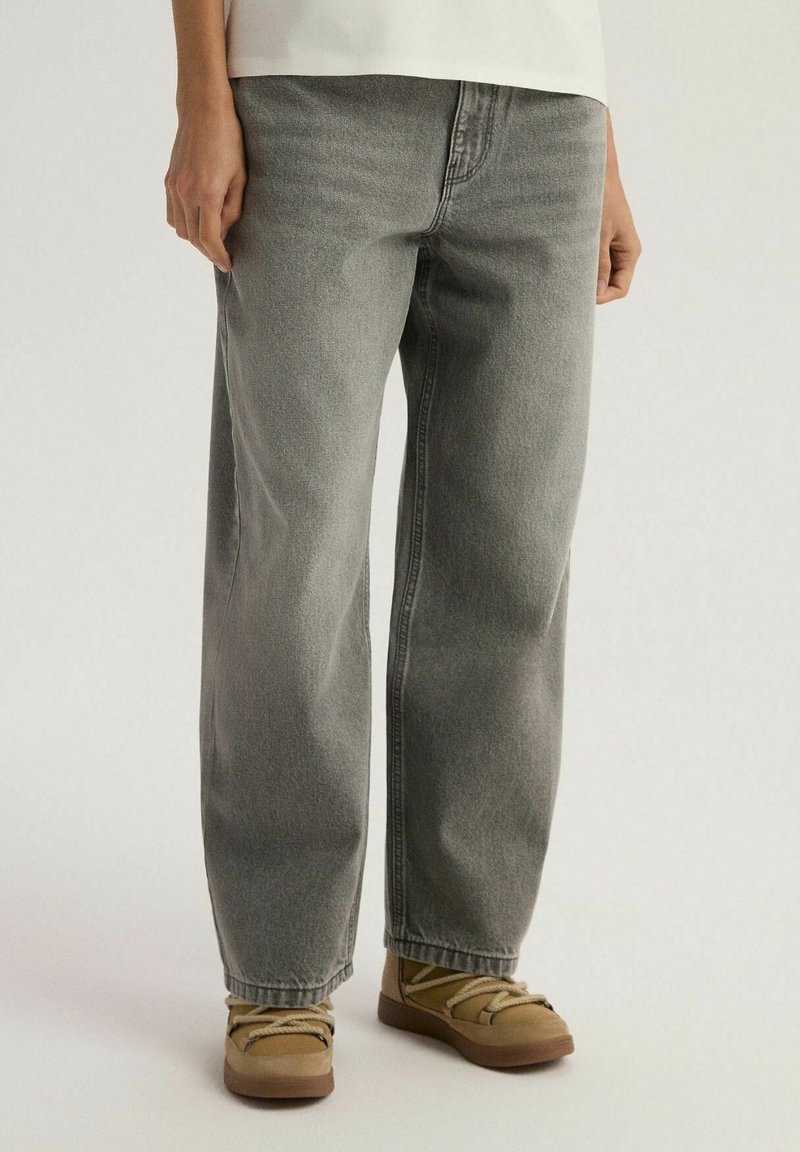 Szare jeansy o średnim stanem, prostym kroju, z lekko wyblakłym wykończeniem i minimalnymi detalami przyszycia. Noszone z jasnobrązowymi, trwałymi butami.