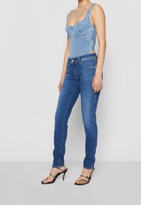 Světle modrý denimový body s výstřihem do kulata a strukturovaným designem; zkombinovaný s tmavě modrými skinny džínami a černými sandály na podpatku.