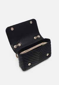 Czarna pikowana torebka ze skóry z złotymi elementami. Otwarta, z kremowym wnętrzem, posiada łańcuszek jako pasek oraz klapę z zapięciem na zatrzaski.