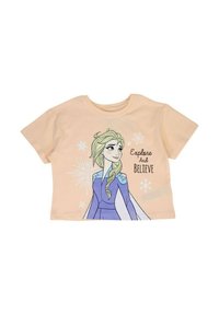 T-shirt en coton couleur pêche avec un graphisme représentant un personnage aux cheveux blonds, portant une robe bleue, accompagné du texte « Explore And Believe » et orné de flocons de neige.