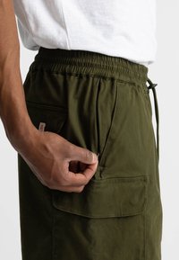 Olijfgroene cargoshorts met een elastische tailleband, voorzien van zijzakken en een kleine patchzak, gemaakt van lichtgewicht stof.