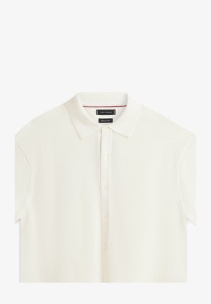 Witte, gebreide polo met korte mouwen, knoopsluiting aan de voorkant en zachte stoffen kraag op een witte achtergrond.