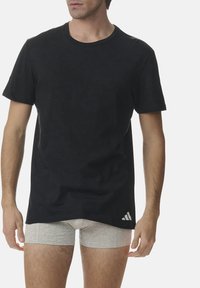 Black cotton T-shirt with short sleeves, round neck, and a subtle pattern, featuring a white Adidas logo on the lower left side.