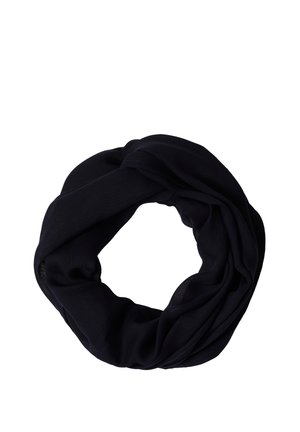 Femme portant une casquette jaune, un t-shirt gris à manches courtes, une écharpe bleue autour du cou et un jean bleu, regardant légèrement sur le côté.